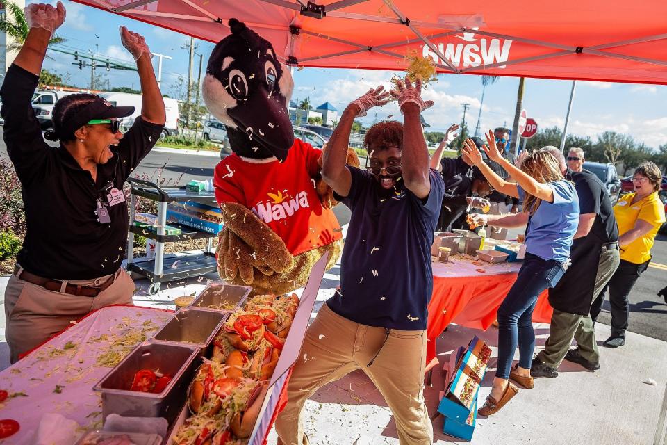 Rosalind "Ms. Ros" McKinnes, West Palm Beach, left, a costumed Wawa mascot Wally, second from left and Sheldon Guy, Coral Springs, center, finish a speed-making sandwich contest with spirited food flinging among competing teams as Wawa personnel celebrated a grand opening with a new store location at 45th Street and Interstate 95 in West Palm Beach, Fla., on February 9, 2023.