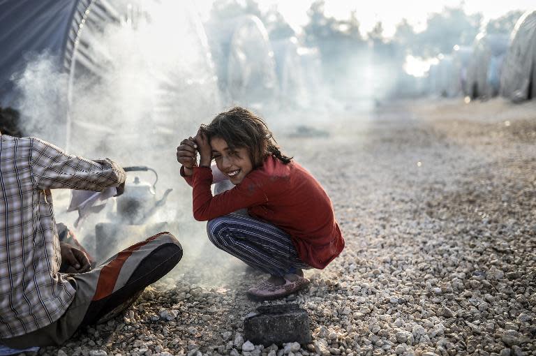 A Kurdish girl smiles as she makes tea outside a tent in the Rojava refugee camp in Suruc, Sanliurfa province, near the besieged Syrian town of Kobane, also known as Ain al-Arab, on October 26, 2014