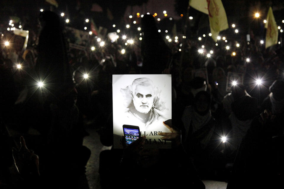A Shiite Muslim illuminates a portrait of Iranian Revolutionary Guard Gen. Qassem Soleimani, with light from a mobile phone, during a rally to condemn his killing in Iraq by a U.S. airstrike, in Karachi, Pakistan, Sunday, Jan. 5, 2020. Iran has vowed 