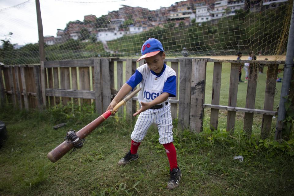 In this Aug. 12, 2019 photo, a boy swings a baseball bat using a donut to loosen his muscles during a practice session at the Brisas de Petare Sports Center in Caracas, Venezuela. More than 100 boys train daily on the baseball field using old bats, balls and gloves, in hopes of achieving a professional baseball career in the United States. (AP Photo/Ariana Cubillos)