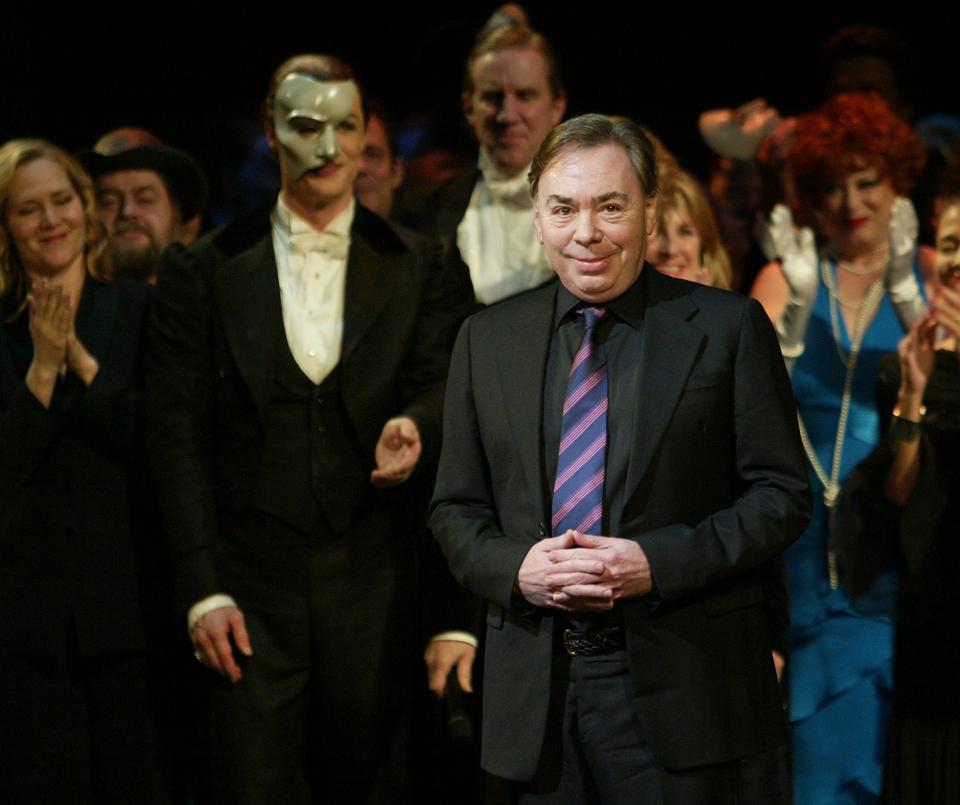 Andrew Lloyd Webber clasps his hands in a black suit and striped tie