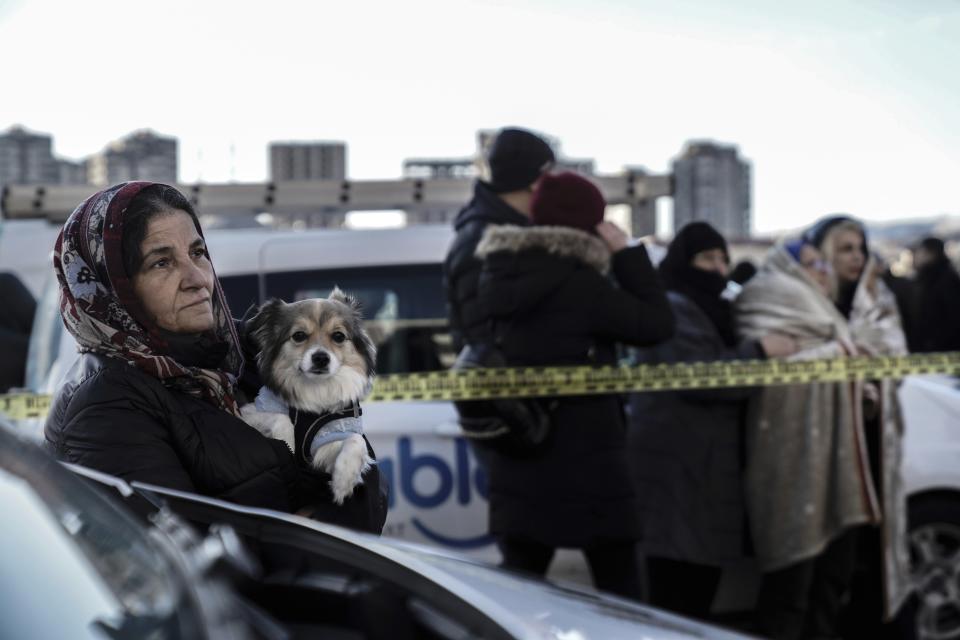 A woman holding a dog watches, the emergency teams as they search for survivors in the rubble of a destroyed building in Gaziantep, southeastern Turkey, Tuesday, Feb. 7, 2023. Search teams and emergency aid from around the world poured into Turkey and Syria on Tuesday as rescuers working in freezing temperatures dug — sometimes with their bare hands — through the remains of buildings flattened by a powerful earthquake. (AP Photo/Mustafa Karali)