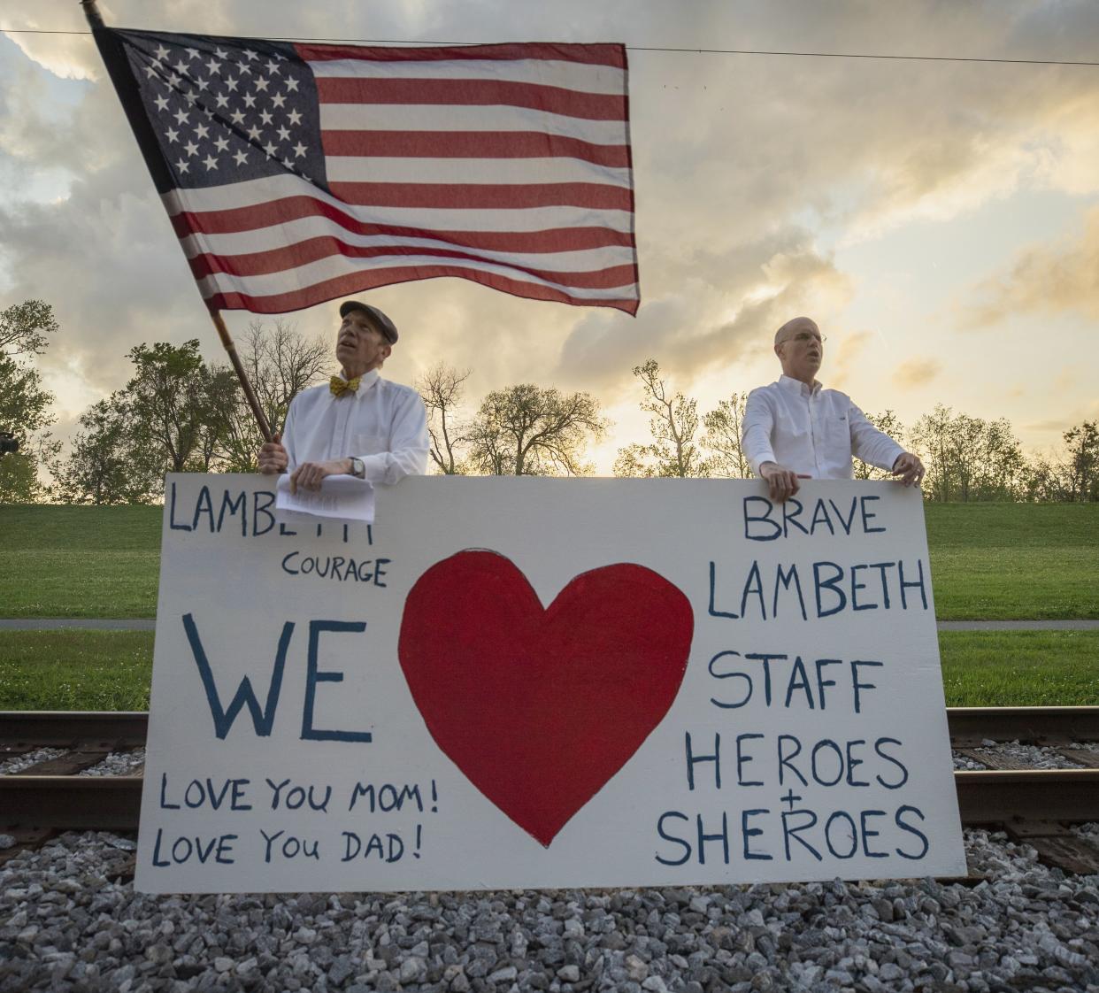 Richard Bienvenu, left, and Tommy Mason, show love and support for Tommy's mother, Lambeth House resident Pat Mason, 83, who is quarantined but with no coronavirus systems, Thursday, March 19, 2020  in New Orleans. Gov. John Bel Edwards said Thursday that a growing number of new coronavirus cases could push Louisiana past its capacity to deliver health care in as few as seven days, comparing the state's possible situation to that of Italy, where the virus has overwhelmed hospitals.