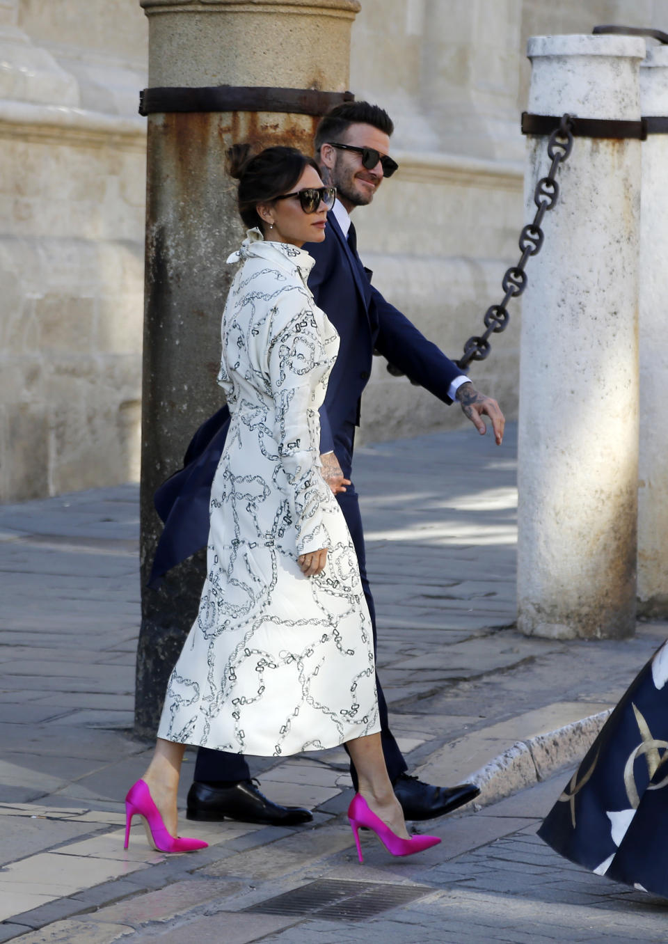 David Beckham, wearing a black suit, and Victoria Beckham, wearing a white dress with patterns and hot pink stilettos, attend the wedding of Real Madrid football player Sergio Ramos and Tv presenter Pilar Rubio at Seville's Cathedral on June 15, 2019 in Seville, Spain