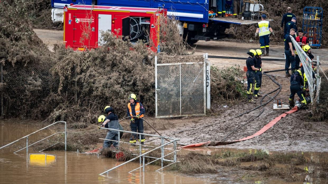 Helfer von Feuerwehr und Technischem Hilfswerk (THW) pumpen Wasser aus einem Regenrückhaltebecken ab, in dem sich noch Fahrzeuge befinden sollen.