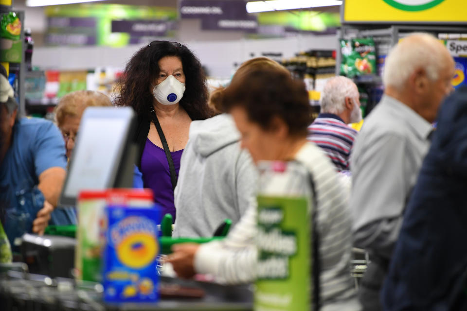 A photo shows a woman wearing a face mask amid a crowd of people inside a Woolworths shopping centre.