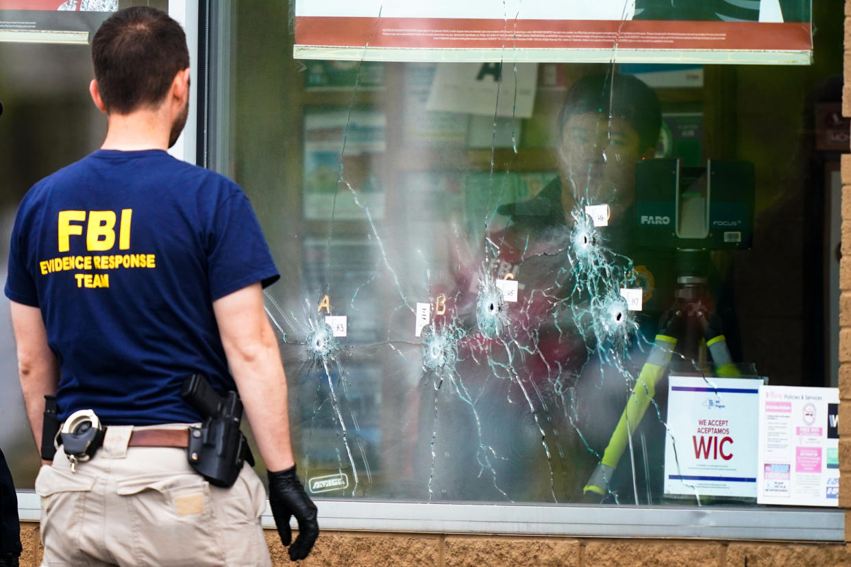A person in an FBI shirt looks at a window in which labeled bullet holes are visible.