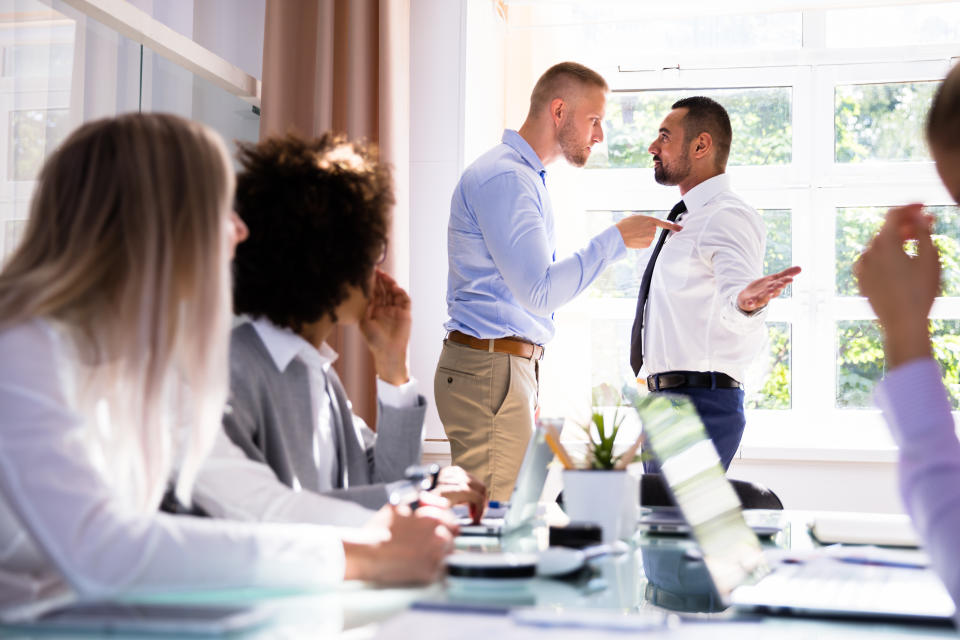 Stressed Businesspeople Sitting In Front Of Two Colleagues Fighting In Office