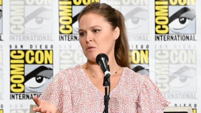 Ronda Rousey speaks on a microphone at a comic con event