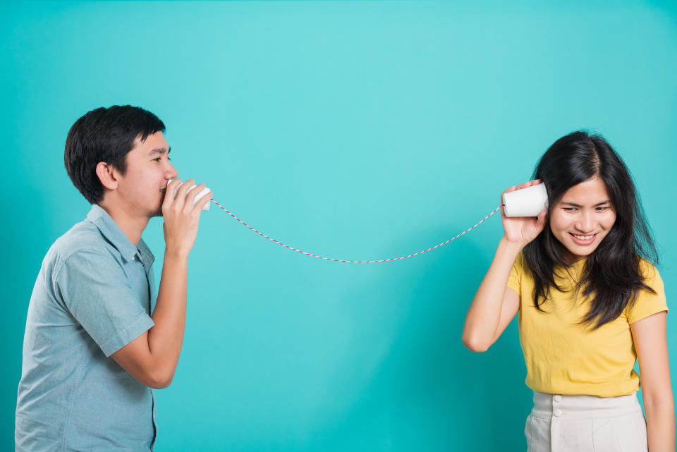 Happy young couple smile and talking together with paper cup telephone. (Photo: Getty Images)