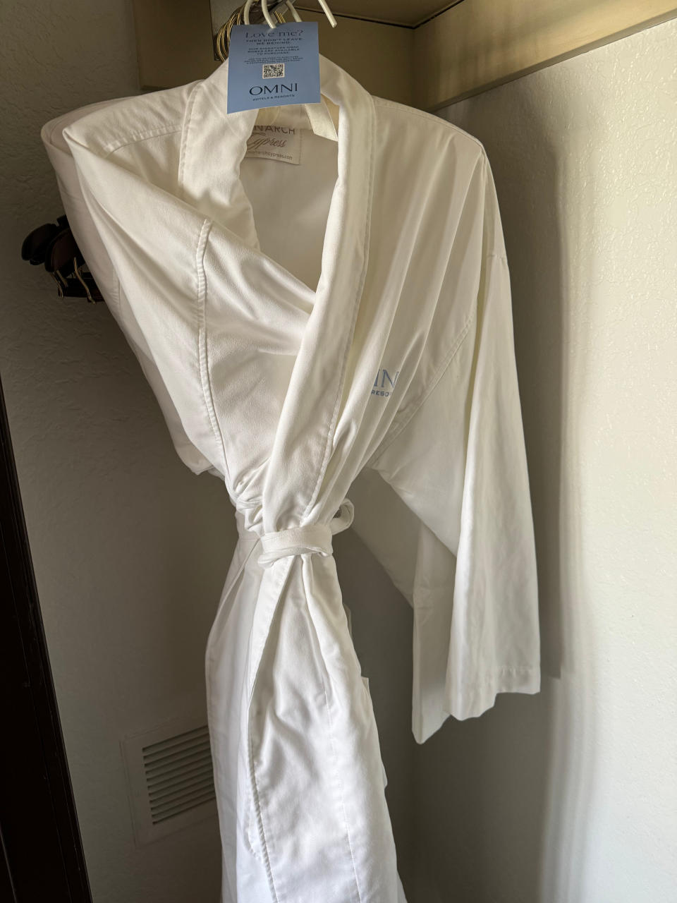 White bathrobe with "Omni" brand logo hanging on a door, possibly from a hotel room