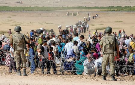 Turkish soldiers stand guard as Syrian Kurds wait behind the border fence to cross into Turkey near the southeastern town of Suruc in Sanliurfa province, September 19, 2014. REUTERS/Stringer