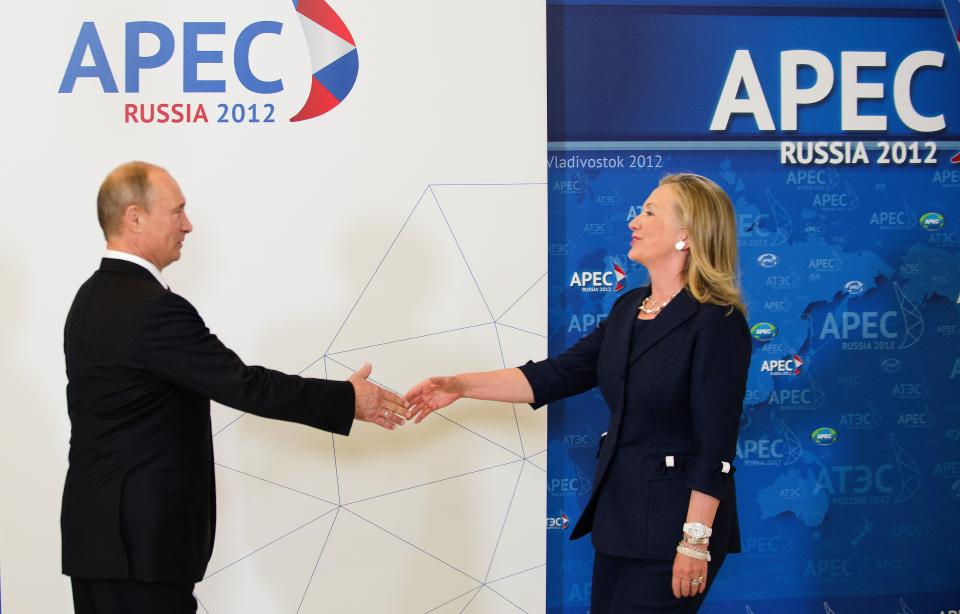 Vladimir Putin shakes hands with Hillary Clinton in front of a backdrop that reads: APEC Russia 2012.