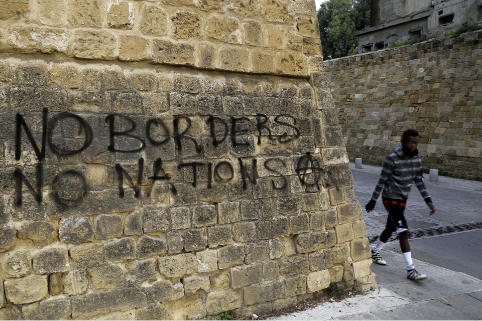 In this Wednesday, Nov. 28, 2018, a migrant walks past graffiti at the UN buffer zone in central Nicosia, Cyprus. The Cyprus Refugee Council, a nonprofit group, said there is now a backlog of about 8,000 asylum applications as of late 2018, and it takes three to five years to process each claim, including appeals.(AP Photo/Petros Karadjias)