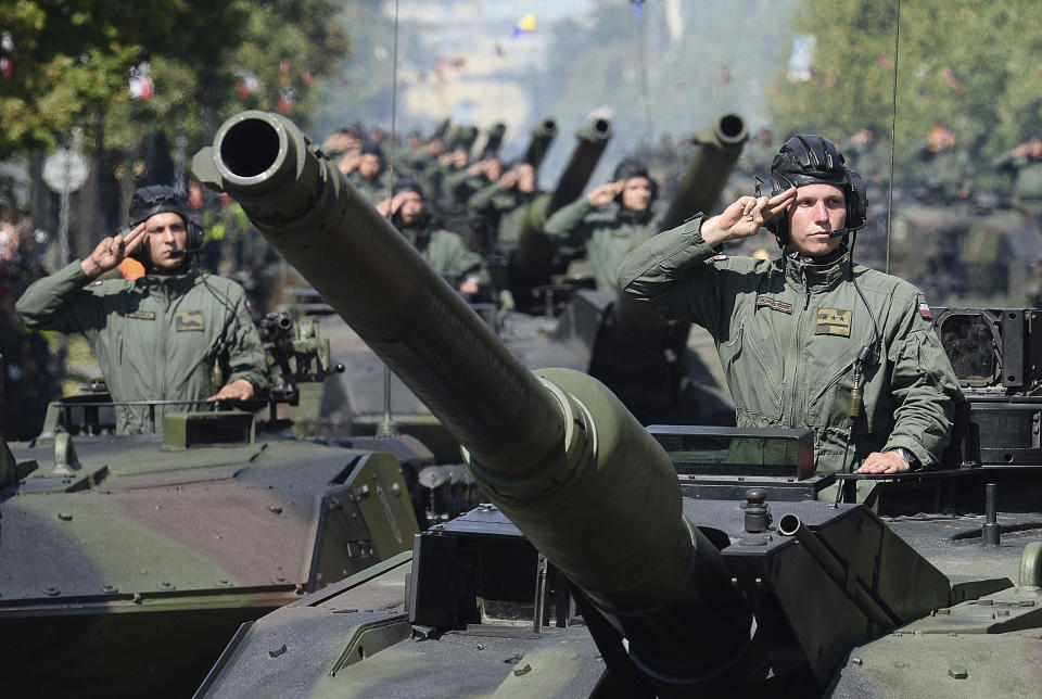 FILE - In this file photo taken Aug.15, 2017 in Warsaw, Poland, Polish Army tank troops salute as their tanks roll on one of the city's main streets during a yearly military parade celebrating the Polish Army Day. Defense Minister Mariusz Blaszczak says Poland will boost its military presence in the east with the formation of a new division of the armed forces. (AP Photo/Alik Keplicz, file)