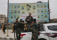 FILE -- In this photo taken on Wednesday, March 28, 2018, members of the Kurdish internal security forces stand on their vehicle in front of a giant poster showing portraits of fighters killed fighting against the Islamic State group, in Manbij, north Syria. The planned U.S. troop withdrawal opens a void in the north and east of Syria, and the conflicts and rivalries among all the powers in the Middle East are converging to fill it. (AP Photo/Hussein Malla, File)