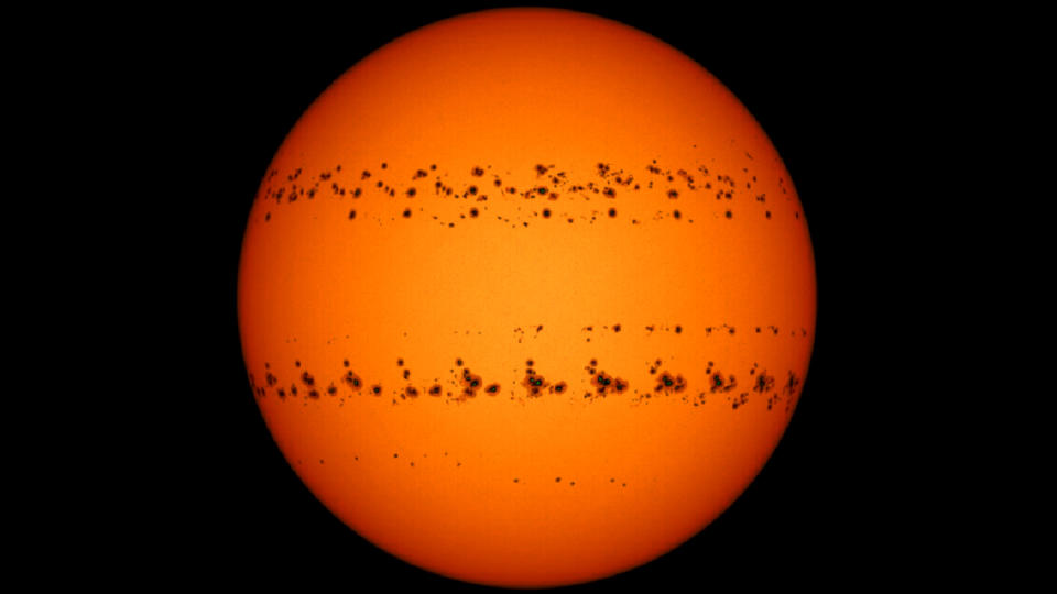 Two bands of dark sunspots stretch across an orange sun on a black background