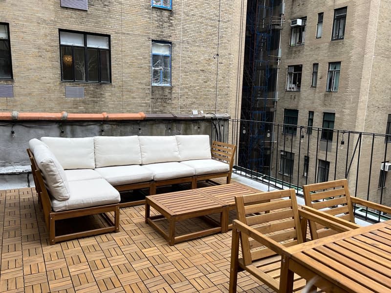Slatted wood dining table and chairs, coffee table, and wood sectional with cushions on rooftop deck with wood flooring.