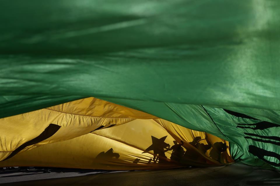 The shadows of demonstrators are cast on a Brazilian flag during a protest demanding the impeachment of Brazilian President Jair Bolsonaro at the Esplanade of Ministries in Brasilia, Brazil, Saturday, July 24, 2021. Activists called for nationwide demonstrations against Bolsonaro to call for his impeachment amid allegations of potential corruption in the Health Ministry's purchase of COVID-19 vaccines and his handling of the pandemic. (AP Photo/Eraldo Peres)