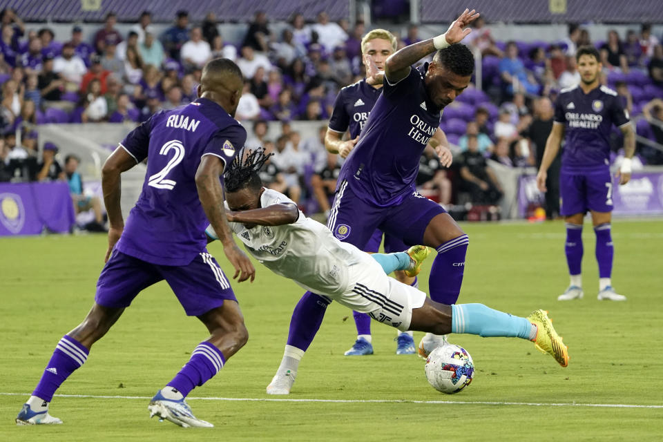 New England Revolution's DeJuan Jones, center, falls as he tries to move between Orlando City's Ruan (2) and Junior Urso, right, during the first half of an MLS soccer match, Saturday, Aug. 6, 2022, in Orlando, Fla. (AP Photo/John Raoux)
