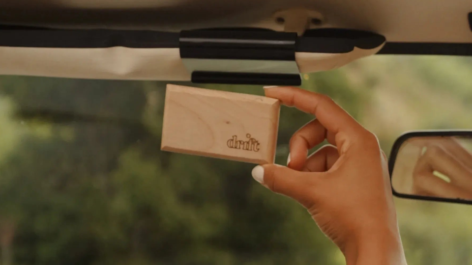 woman holding up wooden Drift air freshener block inside car