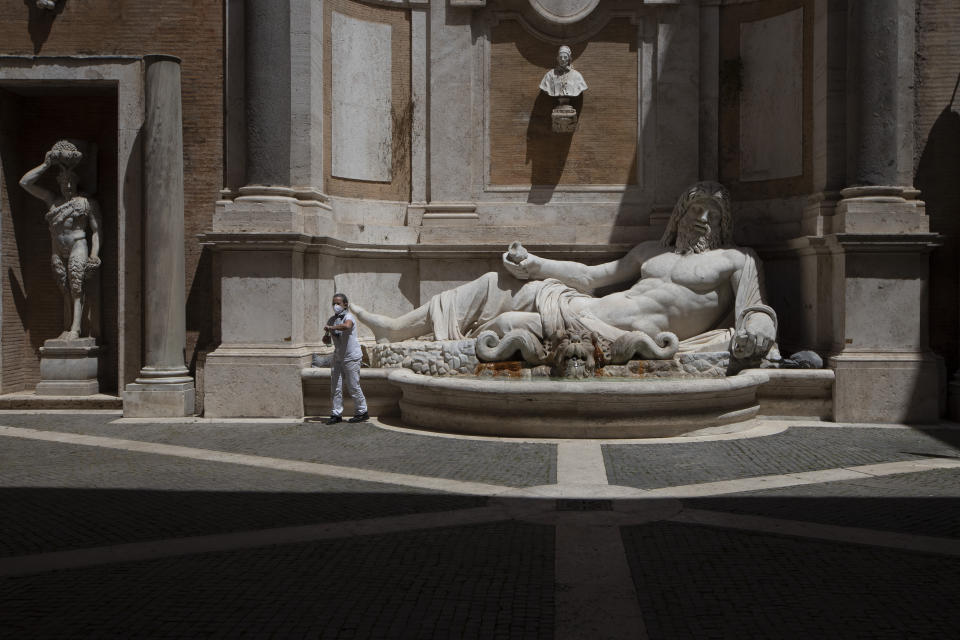 A museum employee wearing a face mask to prevent the spread of COVID-19 fills a bottle at a fountain next to the 3rd century marble statue known as Marforio, at Rome's Capitoline Museums, Tuesday, May 19, 2020. In Italy, museums were allowed to reopen this week for the first time since early March, but few were able to receive visitors immediately as management continued working to implement social distancing and hygiene measures, as well as reservation systems to stagger visits to museums in the onetime epicenter of the European pandemic. (AP Photo/Alessandra Tarantino)