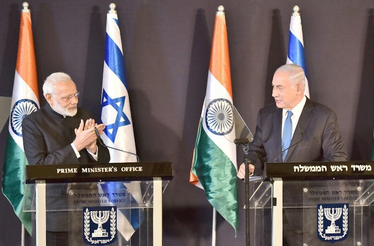 Narendra Modi and Benjamin Netanyahu facing each other on a stage in front of Indian and Israeli flags.