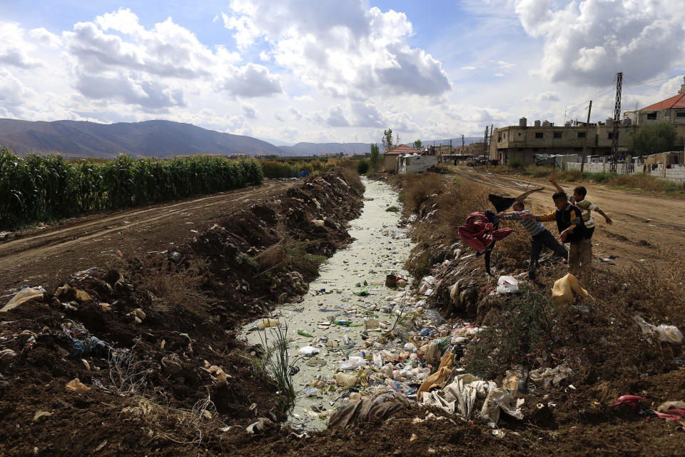 FILE - Syrian refugee boys throw trash into sewage water at a Syrian refugee camp in the town of Hosh Hareem, in the Bekaa valley, east Lebanon, Wednesday, Oct. 28, 2015. Against the backdrop of a worsening economic crisis and political stalemate, Lebanese officials have launched a crackdown on the country's Syrian refugees. (AP Photo/Hassan Ammar, File)