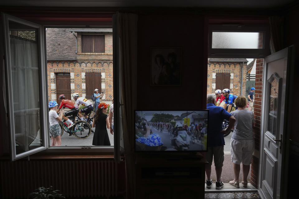 Claudette, right, and Jacky Lemeije stand in the doorway of their house as the pack with Slovenia's Tadej Pogacar, wearing the overall leader's yellow jersey, right, passes through the village of Ligny-le-Ribault during the tenth stage of the Tour de France cycling race over 187.3 kilometers (116.4 miles) with start in Orleans and finish in Saint-Amand-Montrond, France, Tuesday, July 9, 2024. (AP Photo/Daniel Cole)