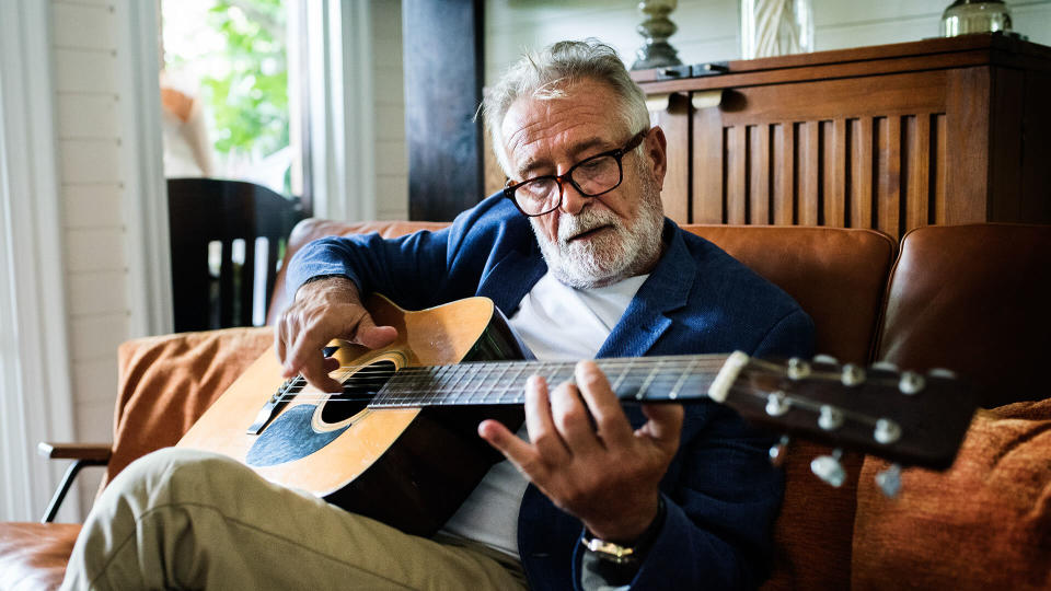 An elderly man is playing guitar.