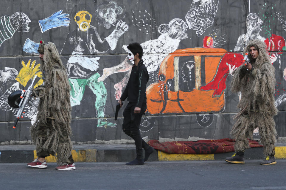 In this Sunday, Nov. 17, 2019 photo, protesters wear camouflage sniper uniforms and hold toy guns as they pass by graffiti at the Saadoun Tunnel, in Baghdad, Iraq. The tunnel that passes under Baghdad’s landmark Tahrir Square has become an ad hoc museum for Iraq's revolution: Young artists draw images and murals that illustrate the country’s tortured past, and the Iraq they aspire to. (AP Photo/Hadi Mizban)