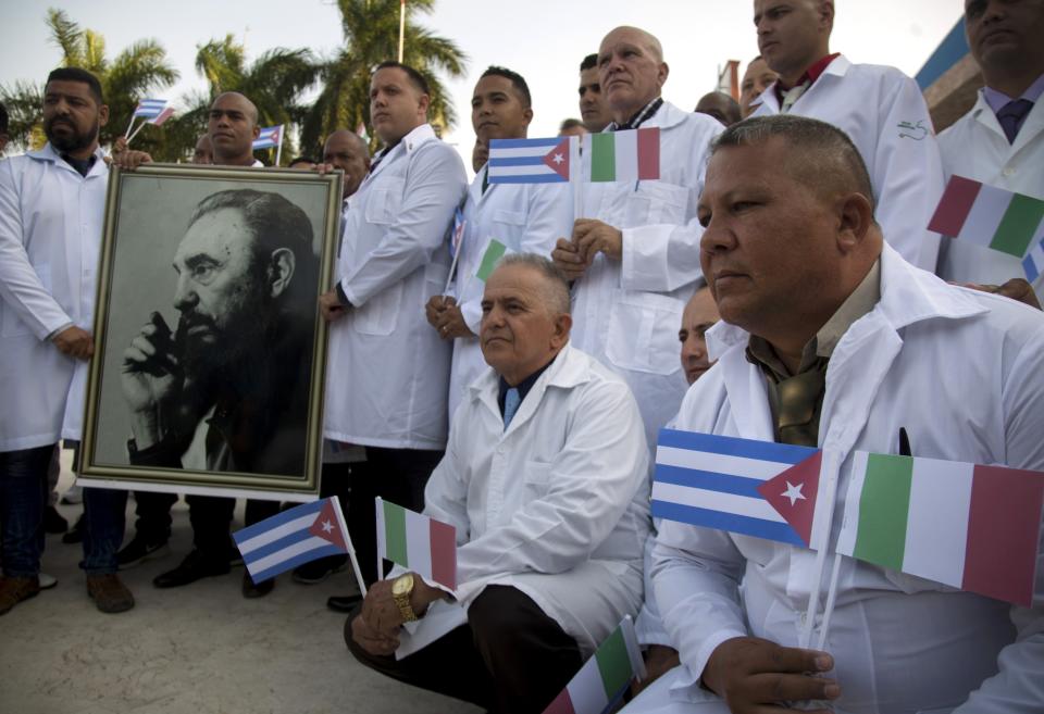 Varios de los médicos y profesionales médicos cubanos que partirán a Italia para ayudar con la pandemia en el país posan para los medios con una foto de Fidel Castro y banderas de Italia y Cuba, en La Habana, Cuba, el sábado 21 de marzo de 2020. (AP Foto / Ismael Francisco)