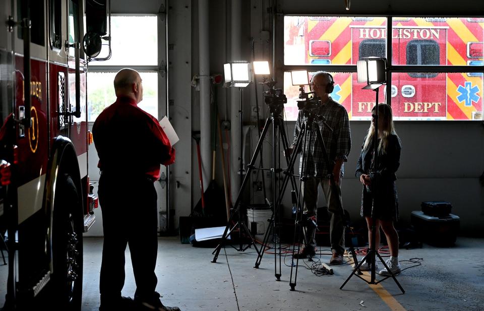 Holliston Fire Chief Michael Cassidy, left, tapes a reading of "Firefighter Nozzelhead Goes to Mexico" for Holliston Cable Access Television (HCAT) station manager Bruce Gilfoy, center, and HCAT intern Shealyn Marino, at the Central Street fire station, May 25, 2022.