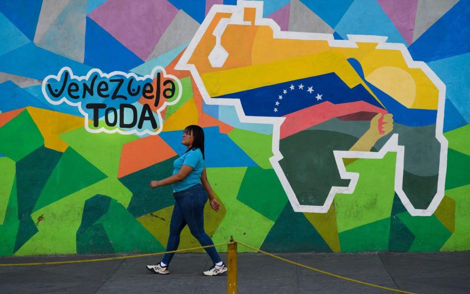 A pedestrian walks past a mural that reads "All of Venezuela" alongside a map depicting the disputed Essequibo territory as part of Venezuela