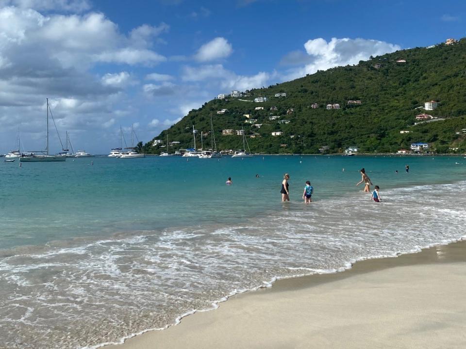 people swimming in the ocean off a beach in the Caribbean with boats out farther in the water