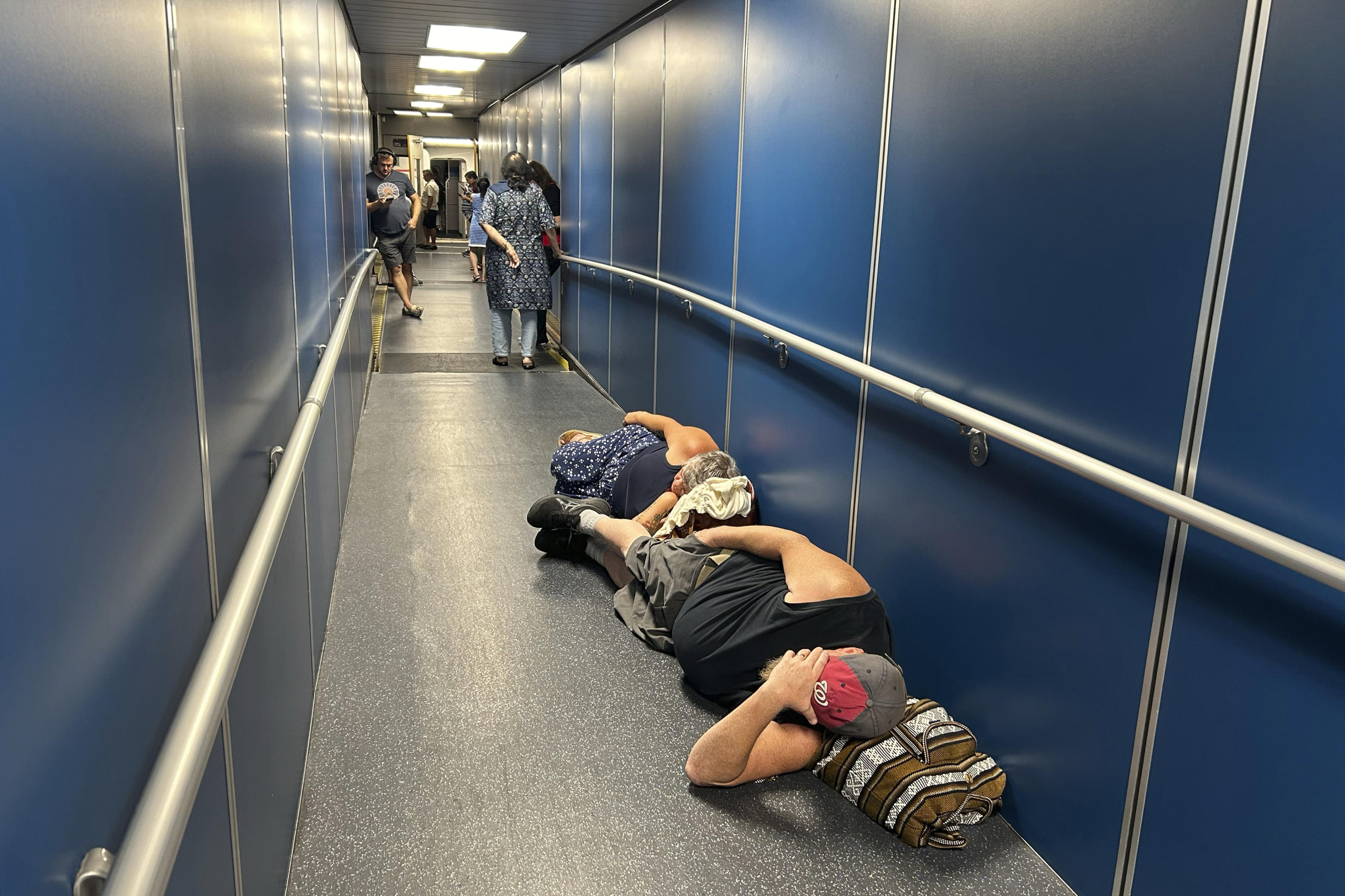 Two travelers at Los Angeles International Airport sleep in a jetway.