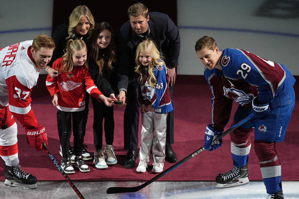 Retired NHL defenseman Darren Helm is joined by his wife and daughters in dropping a ceremonial puck during a ceremony to honor Helm's career before the first period of an NHL hockey game Wednesday, March 6, 2024, in Denver. Detroit Red Wings left wing J.T. Compher, far left, and Colorado Avalanche center Nathan MacKinnon, far right, took part in the face off. Helm played most of his career with the Red Wings before winning the Stanley Cup as a member of the Avalanche in 2022. (AP Photo/David Zalubowski)