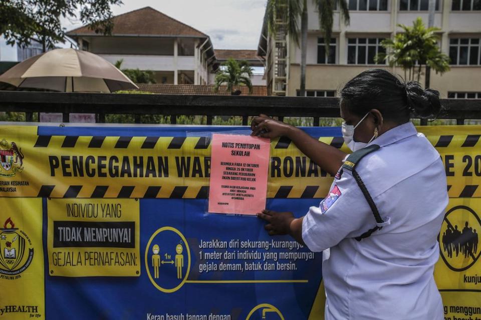 A security guard attaches a notice of closure to the gate of Sekolah Menengah Kebangsaan Bandar Utama Damansara 4 in Petaling Jaya October 12, 2020. — Picture by Hari Anggara