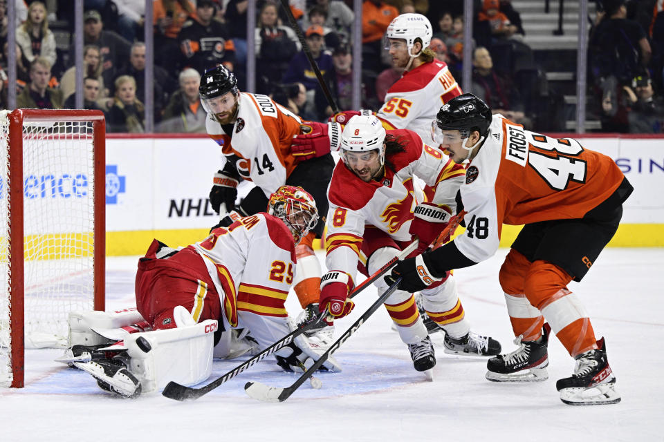 Calgary Flames goaltender Jacob Markstrom (25) makes a save as Chris Tanev (8) and Philadelphia Flyers' Morgan Frost (48) reach for the puck during the second period of an NHL hockey game, Saturday, Jan. 6, 2024, in Philadelphia. (AP Photo/Derik Hamilton)