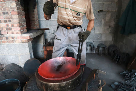 A blacksmith hammers a wok at a workshop for handmade woks in Datian village, Hubei province, China August 13, 2018. REUTERS/Thomas Suen