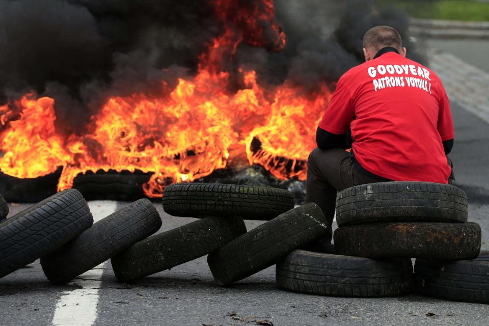 Flames and smoke rise from burning tyres as a worker sits on a barricade blocking the entrance of U.S. tyre-maker Goodyear's plant to protest job cuts in Amiens, northern France, in this June 3, 2013 file picture. French trade unionists held two executives overnight on Tuesday January 7, 2014 at the country's Goodyear tyre plant - a flashpoint for France's troubled industrial relations - to demand higher pay-outs for more than a thousand planned layoffs. Workers at the idled factory in the northern city of Amiens have been trying to negotiate redundancy terms with management for nearly a year, after Texan tyre tycoon Maurice Taylor withdrew a potential rescue bid on the grounds that French workers were lazy - triggering a political storm. The message reads "Goodyear - Gangster Bosses". Picture taken June 3, 2013. REUTERS/Benoit Tessier/Files (FRANCE - Tags: BUSINESS INDUSTRIAL EMPLOYMENT)