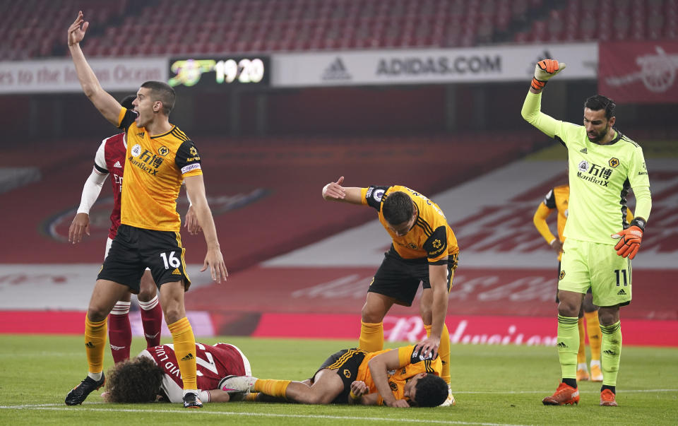 Players gesture to medical staff after a head clash between Arsenal's David Luiz, bottom left, and Wolverhampton Wanderers' Raul Jimenez during the English Premier League soccer match between Arsenal and Wolverhampton Wanderers at Emirates Stadium, London, Sunday, Nov. 29, 2020. (John Walton/Pool via AP)