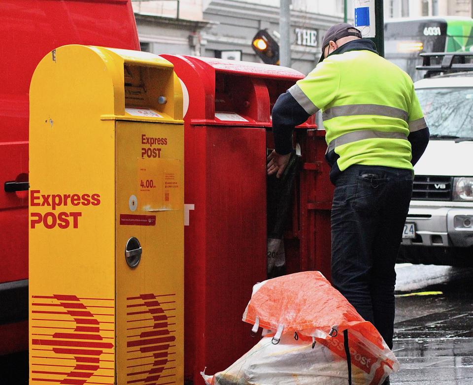 A mailman empties an Australia Post box in rainy conditions. Source: Getty Images