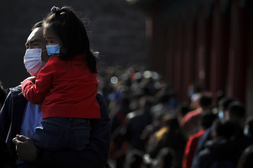 A man holds a child, both wearing face masks to help curb the spread of the coronavirus line up with visitors to enter an exhibition held at the Forbidden City in Beijing, Saturday, Nov. 7, 2020. China on Saturday reported 33 new confirmed coronavirus infections, all of which the National Health Commission said were in patients who contracted the virus abroad. (AP Photo/Andy Wong)