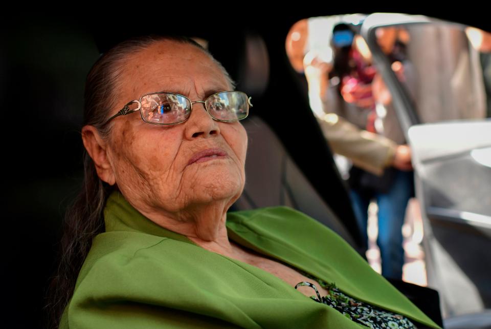 An elderly woman is seen seated in a car and looking out the window.