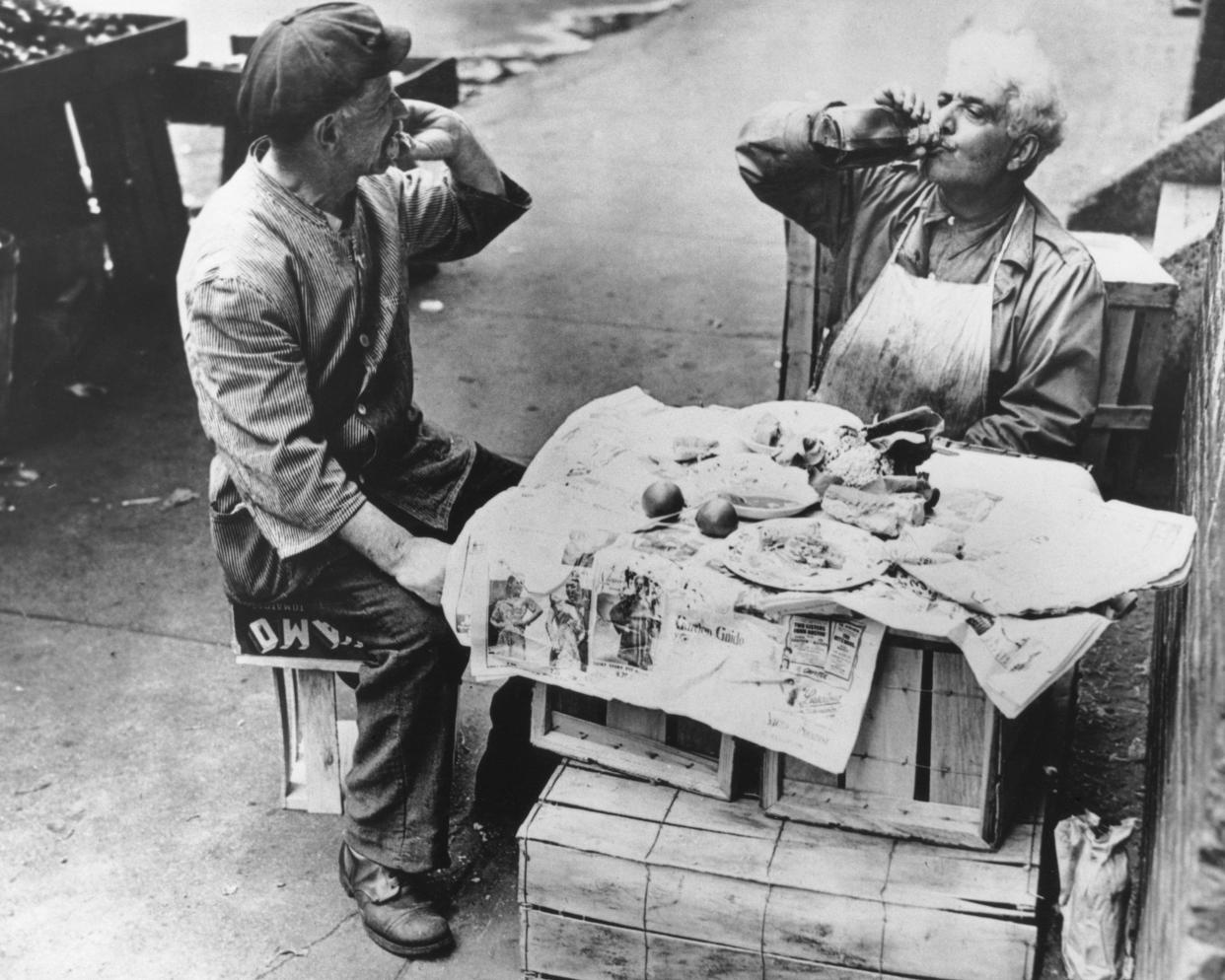 two street vendors have lunch at a makeshift table of wooden crates covered with newspaper, New York, Aug. 1946