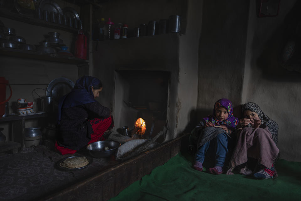 A Kashmiri women prepares bread as her cousins sit near, inside a mud house in Drang village northwest of Srinagar, Indian controlled Kashmir Friday, Dec. 22, 2023. Villages in the hilly areas of Kashmir live in houses made of mud and wood due to their insulating properties, which also help regulate indoor temperatures, keeping the interior warmer during winter. (AP Photo/Dar Yasin)