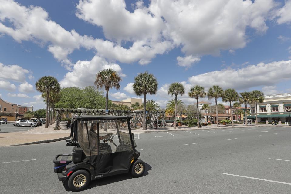 FILE-In this Thursday, March 19, 2020 file photo, a resident drives his golf cart down what usually is a busy street by the Spanish Springs town square in The Villages, Fla. (AP Photo/John Raoux, File)