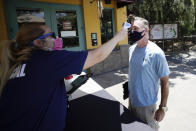 Health services worker Summer Deibert, left, checks the temperature of James McCluskey, right, as he arrives for work before the reopening of the San Diego Zoo, Thursday, June 11, 2020, in San Diego. California's tourism industry is gearing back up with the state giving counties the green light to allow hotels, zoos, aquariums, wine tasting rooms and museums to reopen Friday. (AP Photo/Gregory Bull)