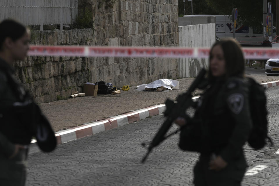 Israeli Border Police secure the scene of a stabbing as the body of a suspected attacker lies covered in Ramle, central Israel, Friday, April 26, 2024. The attack, which Israel's rescue services said was carried out by a militant, injured an 18-year-old woman. Paramedics brought her to the hospital in serious condition. Hebrew media reported that the attacker was shot dead shortly after the stabbing. (AP Photo/Mahmoud Illean)